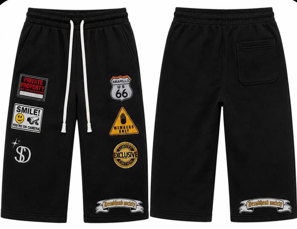 Black sweat shorts shown from the front and back, featuring white drawstrings and multiple graphic patches including Route 66, 'Smile!', 'Private Property', and 'Welcome to Hell' on the front, and matching patches on the back pocket.