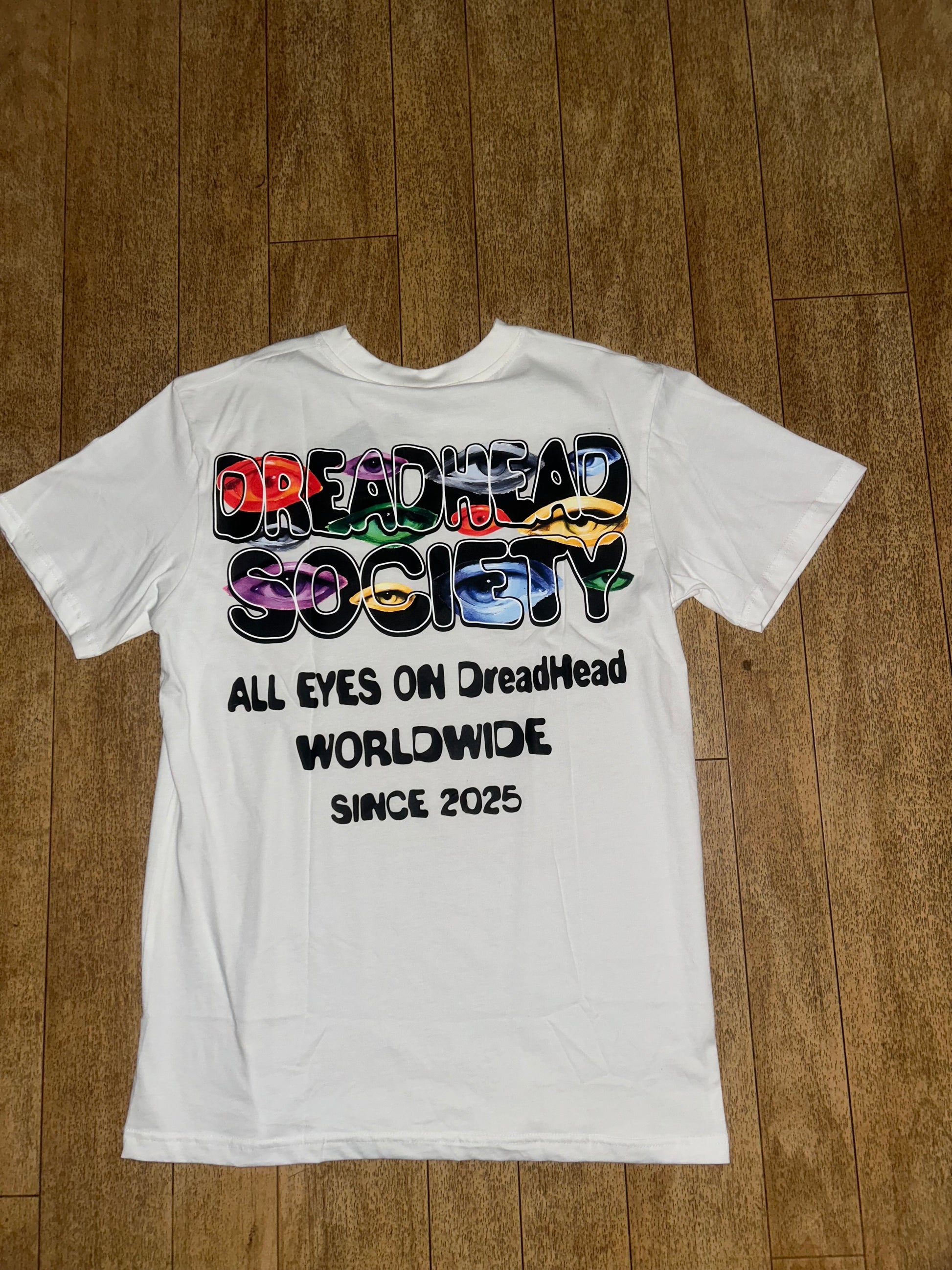 Dreadhead Society Eyes On Us White Graphic Tee Back Graphic View on Wooden Floor